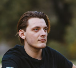 Young man with long hair in a black shirt, outdoors
