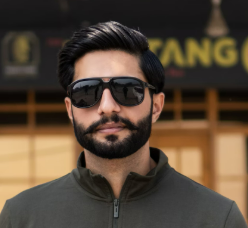 Bearded man in sunglasses and a zip-up sweater, standing confidently